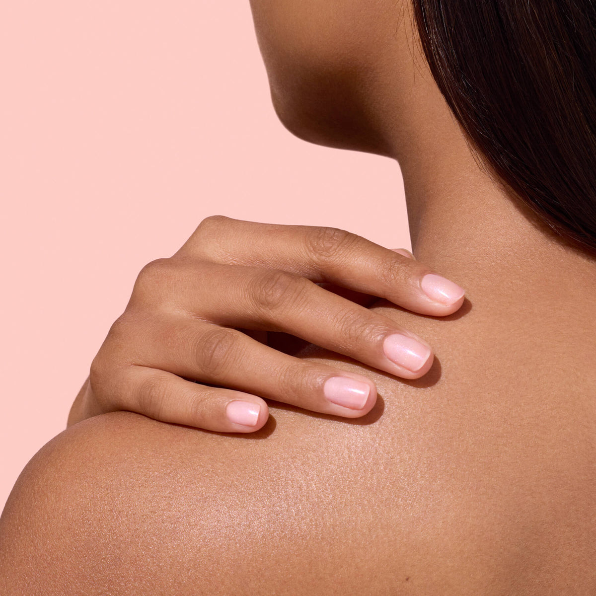 Mano con unghie rosa brillanti su una spalla