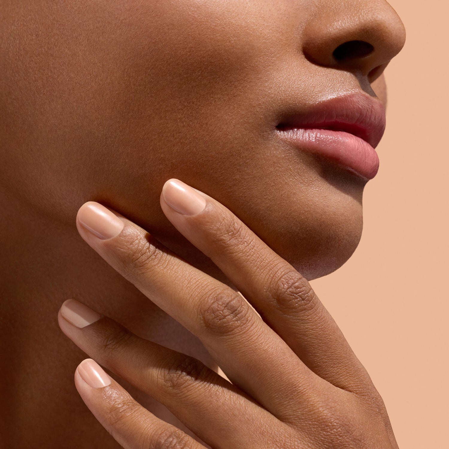 Main aux ongles beige près du menton