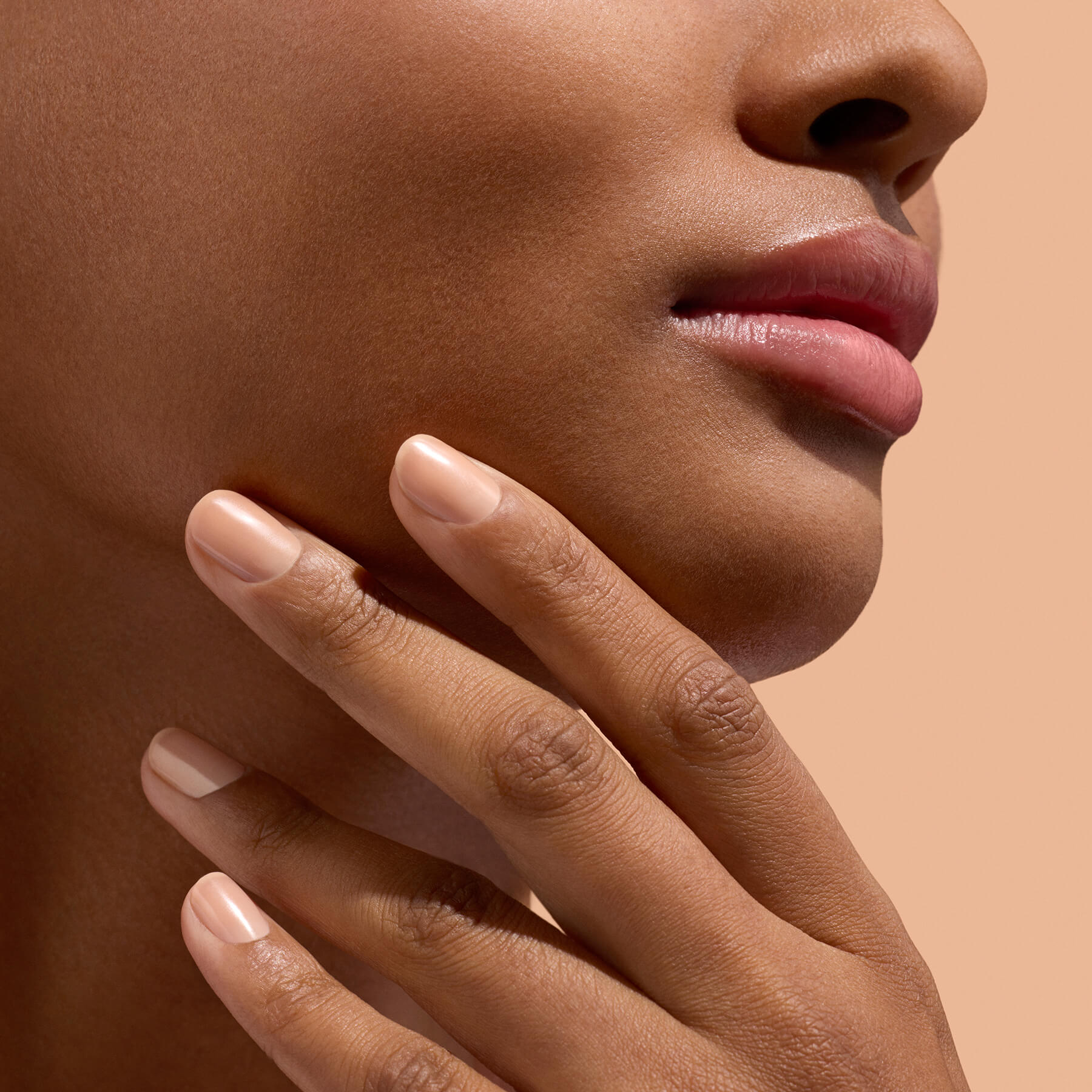 Main aux ongles beige près du menton